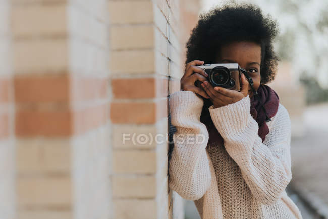 Portrait of girl leaning on brick wall and taking photo with analog camera — Stock Photo