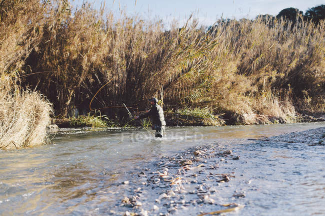 Vue latérale de pêcheur homme debout dans la rivière avec tige — Photo de stock