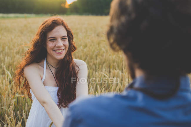 Портрет счастливой рыжеволосой девушки, держащей парней за руки на ржаном поле — стоковое фото