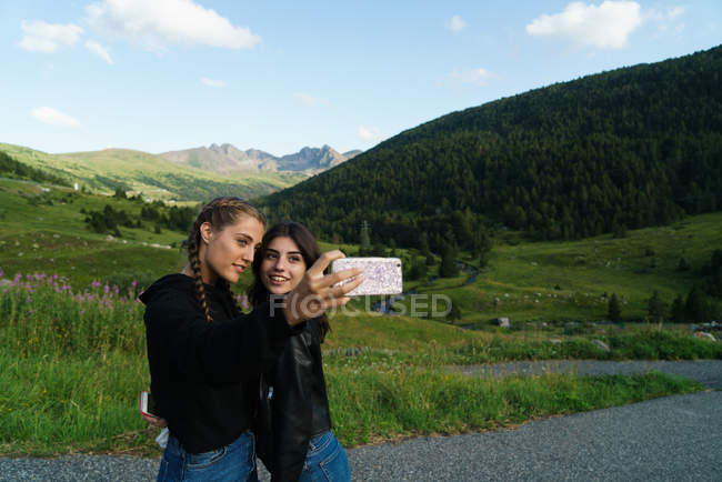 Dos mujeres abrazadas tomando selfie en el prado - foto de stock