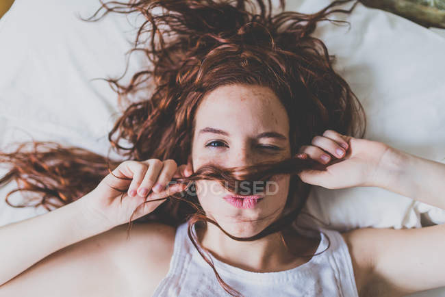 Mulher deitada na cama usando o cabelo como bigode — Fotografia de Stock