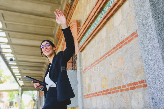 Side view of smiling woman in smart costume holding tablet and waving goodbye. Copyspace — Stock Photo