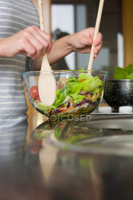 Mujer de la cosecha mezclando ensalada en un tazón en el mostrador de cocina - foto de stock