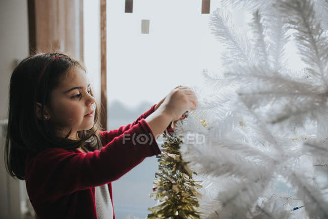 Vista laterale della ragazza sorridente che mette le bagattelle sull'albero di Natale decorativo — Foto stock