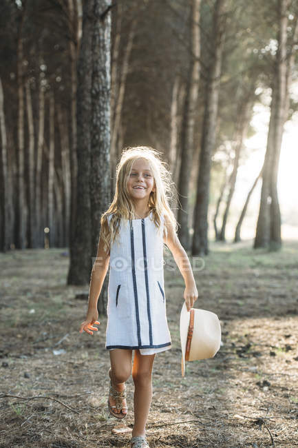 Charming little girl posing with hat at sunlit forest — Stock Photo