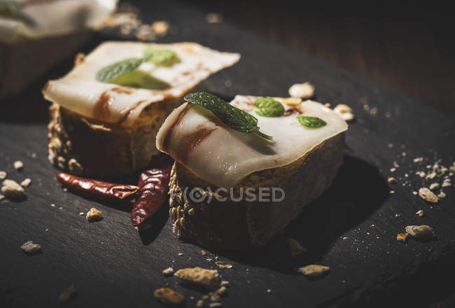 Бутерброды с солоноватым беконом и мятными листьями на доске — стоковое фото
