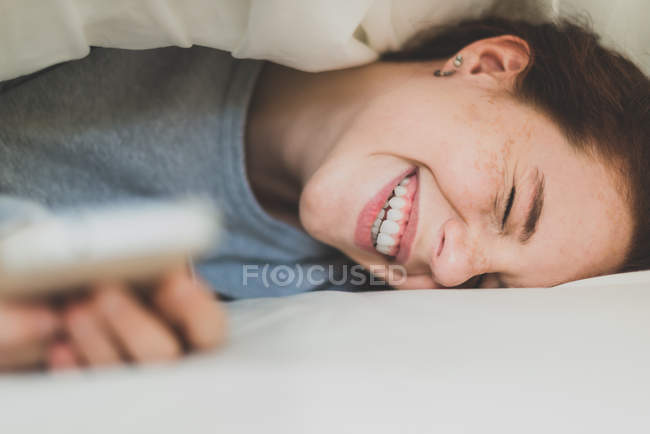 Lachendes Mädchen unter Kopfkissen liegend — Stockfoto