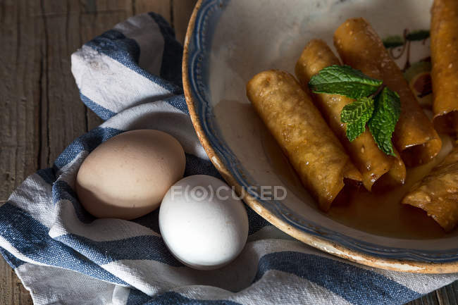 Vista de cerca del plato con tubos de masa de miel frita y palitos de canela en la toalla - foto de stock
