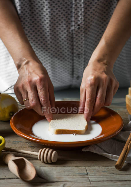 Partie médiane de la tranche de pain trempée femelle dans une assiette avec du lait sur la table — Photo de stock