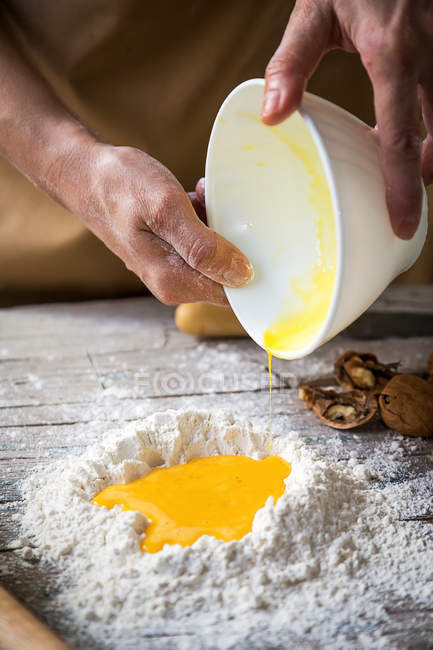 Schnitte Bild der Hände hinzufügen zertrümmerte Eier in Haufen von Mehl auf rustikalen Holztisch — Stockfoto