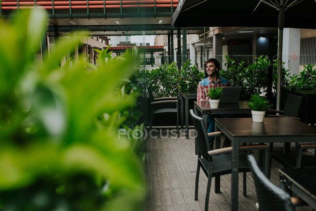 Homme assis dans un café extérieur avec ordinateur portable et regardant de côté — Photo de stock