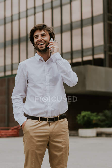 Portrait of smiling businessman in white shirt talking on smartphone at urban scene — Stock Photo