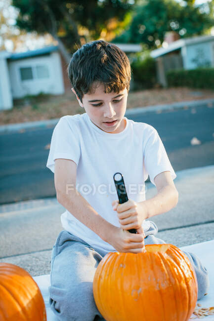 Ragazzo intaglia zucca di Halloween con coltello all'aperto durante il giorno. — Foto stock