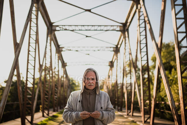 Front view of old man in hoodie standing on bridge and looking at camera. Copyspace — Stock Photo