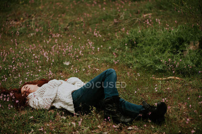 Імбир дівчина лежить на землі з квітучими дикими квітами — стокове фото