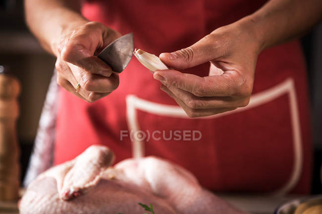 Close-up of female hands peeling garlic clove for preparing roasted chicken — Stock Photo