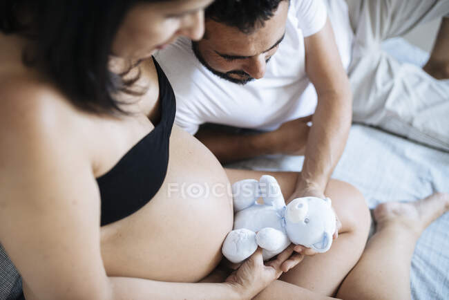 Padres jóvenes esperando por el niño y mirando juguete osito de peluche, para su bebé. - foto de stock