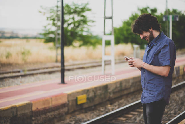 Вид сбоку улыбающегося человека с помощью смартфона на железнодорожной платформе — стоковое фото