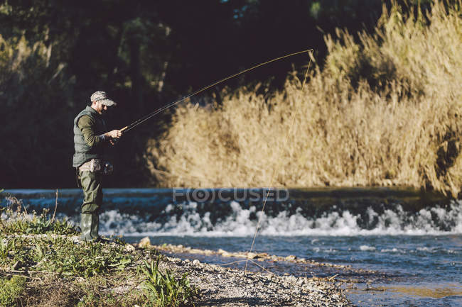 Vista lateral do homem de pé no rio e pesca com vara — Fotografia de Stock