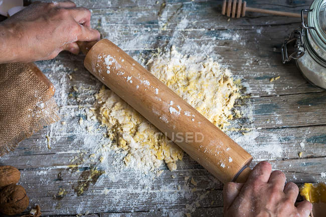 Vue ci-dessus de la pâte à rouler mains avec rouleau à pâtisserie sur table en bois rustique — Photo de stock