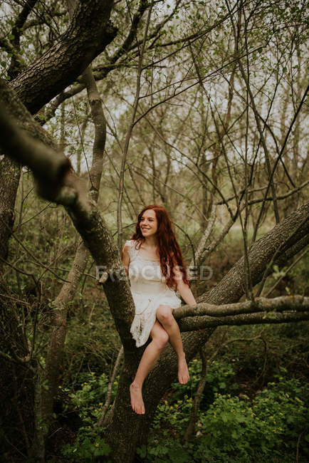 Menina de gengibre posando em flexão sobre ramo de árvore de chão e olhando para o lado — Fotografia de Stock