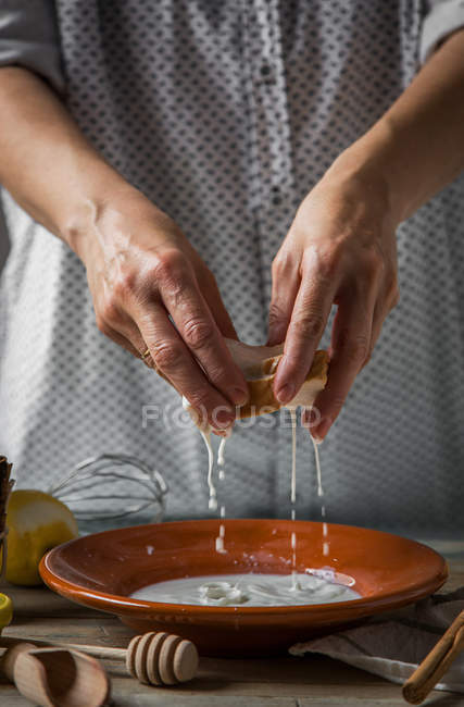 Mid section of female squeezing off bread slice from sweet milk in plate — Stock Photo