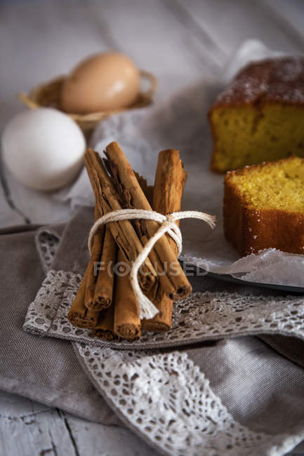 Vue rapprochée de attaché avec une pile de cordes rurales de bâtons de cannelle sur la serviette près du gâteau fait maison et des œufs sur le fond — Photo de stock