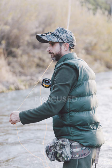 Вид збоку на людину, що стоїть біля річки і риболовля зі стрижнем в осінній день — стокове фото