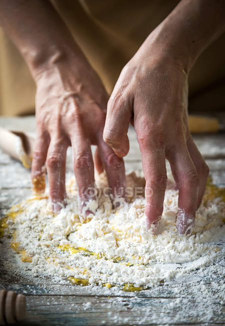 Crop image of hands kneading flour and oil for dough on rural wooden table — Stock Photo