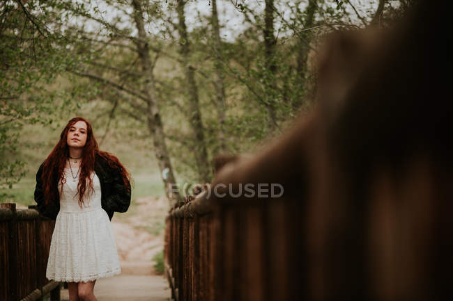 Спокойная рыжая девушка позирует на деревянном мосту в сельской местности — стоковое фото