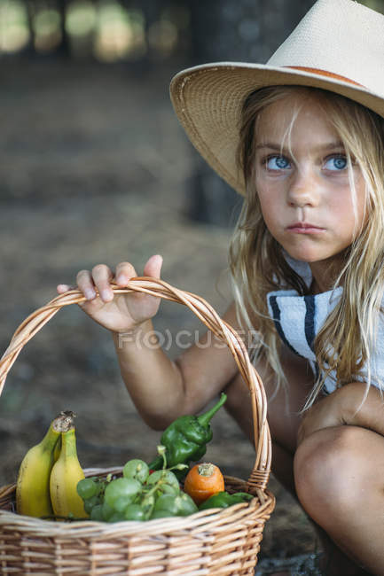 Child in hat holding basket with fruit and looking away — Stock Photo