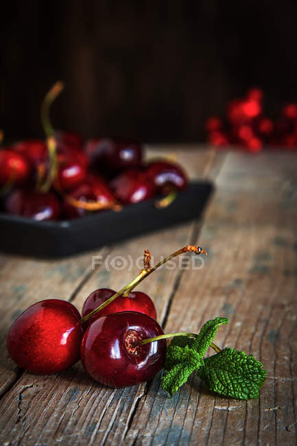 Bodegón de cerezas y hojas de menta sobre mesa de madera - foto de stock