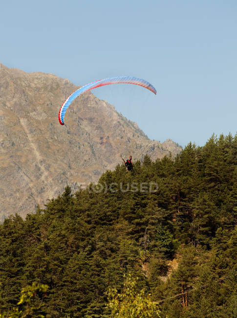 Distant view of person paragliding over forest covered mountains — Stock Photo