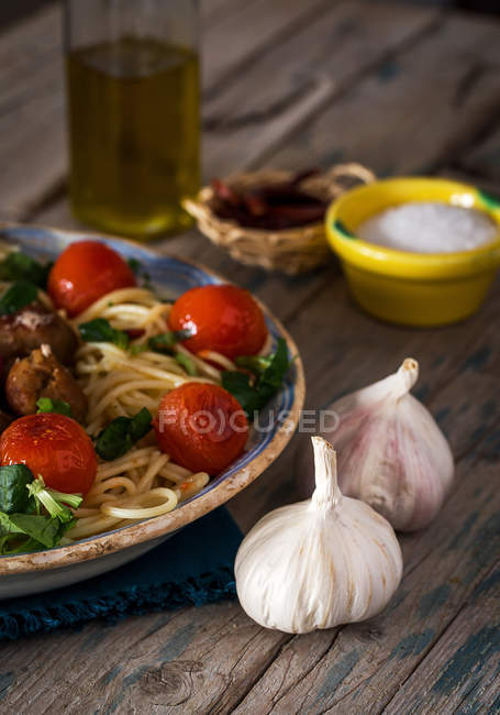 Erntebild eines Tellers voller Pasta mit Basilikum und Kirschtomaten auf rustikalem Holztisch mit Knoblauch und Tellern mit Gewürzen — Stockfoto