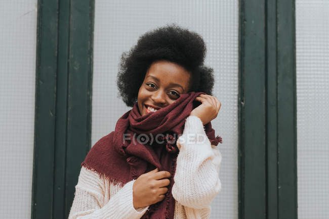Портрет девушки, позирующей с мягким красным шарфом и смотрящей на камеру через стену на заднем плане — стоковое фото