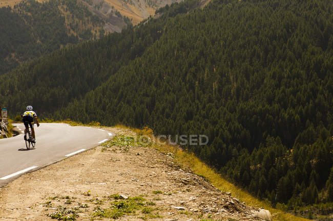 Vue arrière du cycliste roulant sur la route dans les montagnes couvertes de forêts — Photo de stock