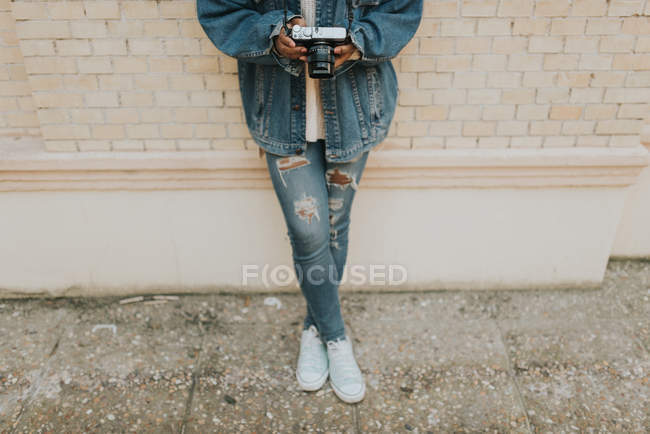 Vue grand angle de la femme portant une caméra analogique et s'appuyant sur un mur de briques — Photo de stock