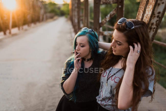 Meninas fumaça conjunta na ponte ao pôr do sol — Fotografia de Stock