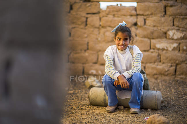 Chica árabe sentada en ruinas y sonriendo - foto de stock