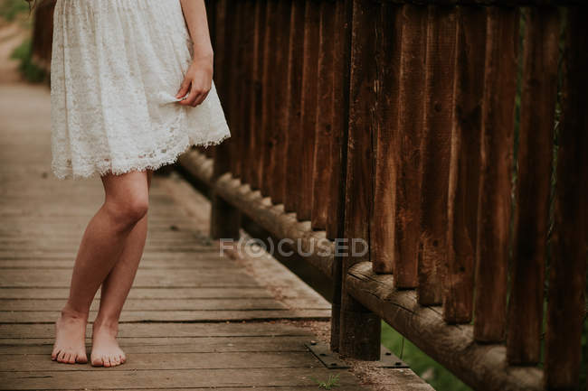 Unterteil eines Mädchens in weißem Kleid, das auf Holzbrücke geht — Stockfoto