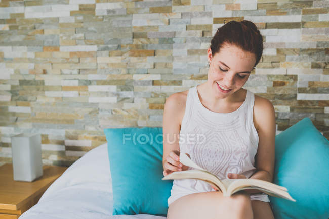 Дівчинка сидить на ліжку і читання книги — стокове фото