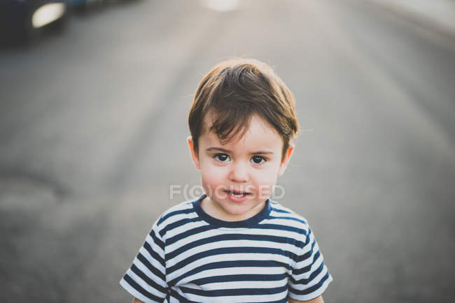 Portrait of lovely boy in striped t-shirts looking at camera on road — Stock Photo