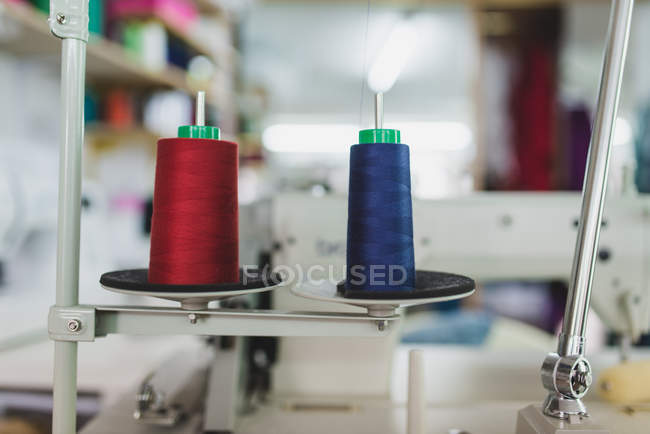 Side view of red and blue spools on spires of sewing machine — Stock Photo