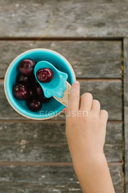 Рука маленькой девочки берет вишню ложкой из миски — стоковое фото
