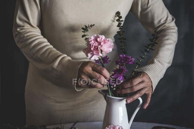 Sección media de floristería femenina colocando flor en jarrón de cerámica blanca en la mesa - foto de stock