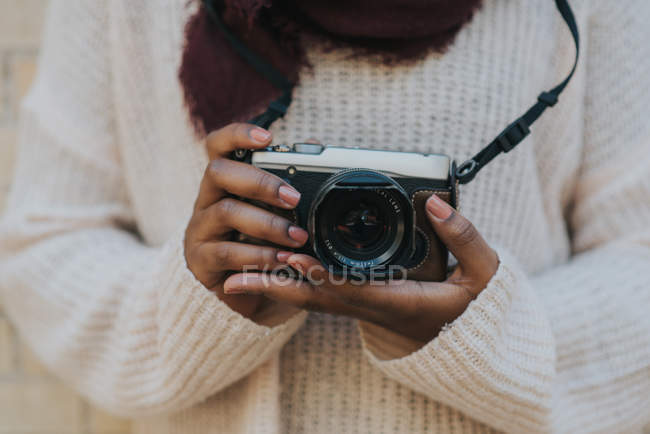 Mid section view of female in casual sweater holding photo camera. — Stock Photo