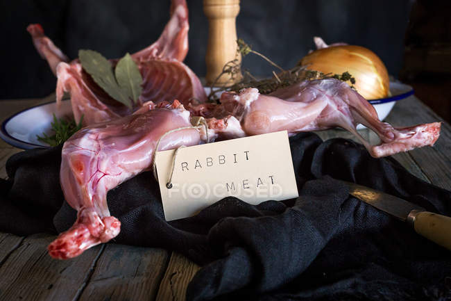 Canal de conejo crudo con ingredientes y etiqueta en la mesa de madera - foto de stock
