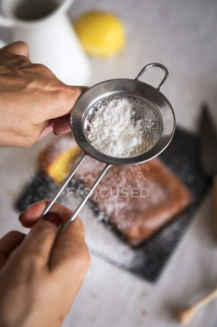 Vista superior de las manos vertiendo azúcar en polvo con colador en la torta - foto de stock