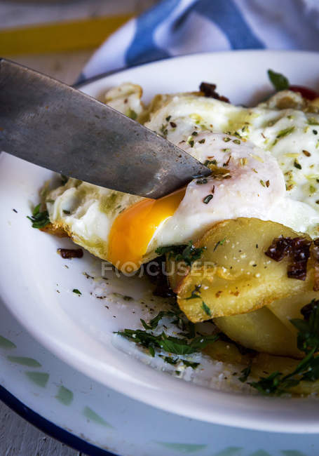 Cerrar cuchillo rebanando huevo frito y patatas - foto de stock