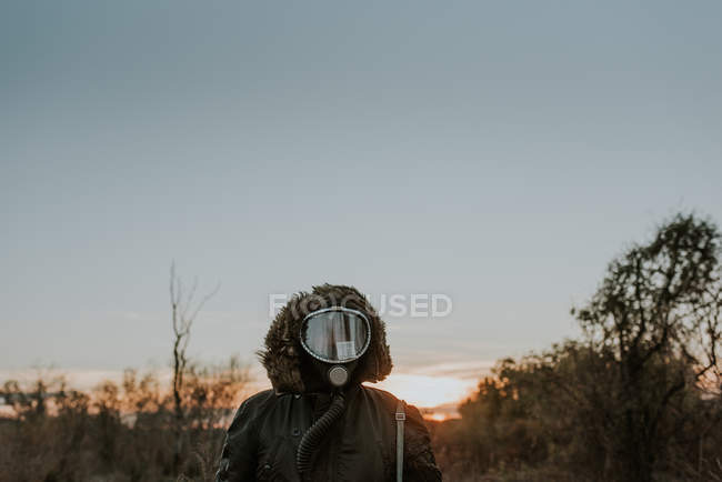 Porträt eines Mannes mit Gasmaske, der bei Sonnenuntergang auf einem Feld steht — Stockfoto